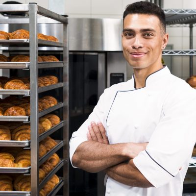 portrait-confident-young-male-baker-front-baked-croissant-shelves